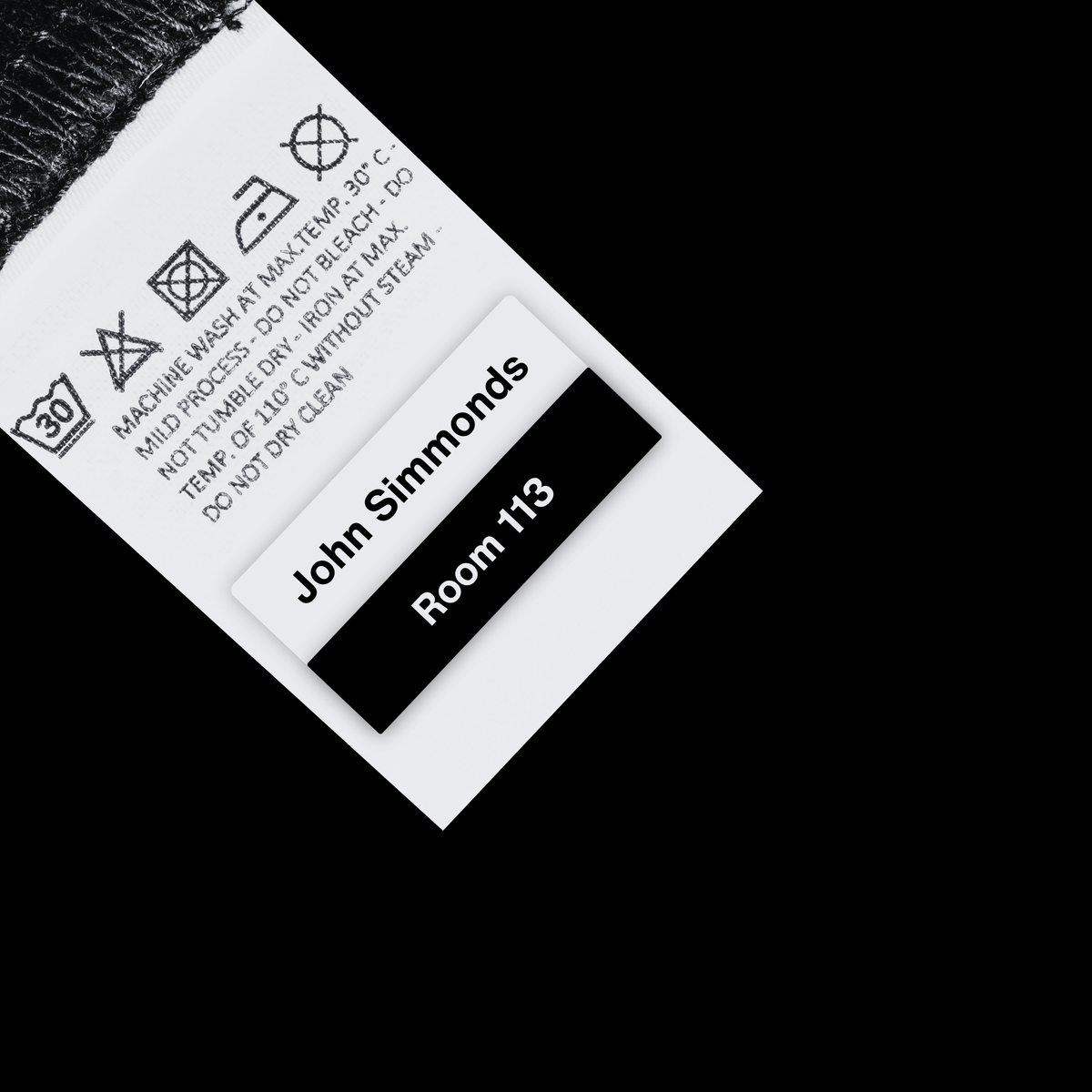 A close-up of a garment care label on a black background. The white label shows washing and drying symbols, care instructions, and the text 'John Simmonds' and 'Room 113'. personalised name tag labels